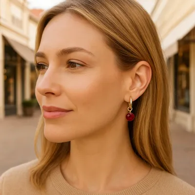 Gold huggie hoop earring with small reflection charm dangling, worn on ear in lifestyle setting
