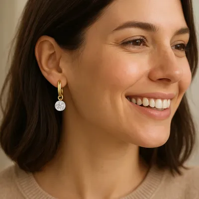 Gold huggie hoop earrings with small charm detail worn in a lifestyle setting, showcasing the delicate reflection design in warm gold tone