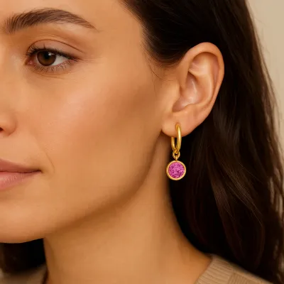 Gold huggie hoop earrings with small reflection charm and October birthstone detail worn in a lifestyle setting