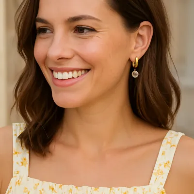 Gold huggie hoop earring with small reflection charm pendant displayed in lifestyle setting