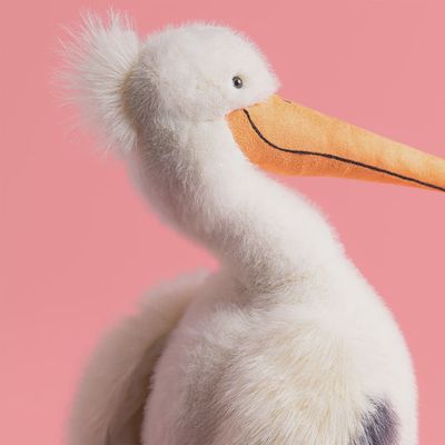 Jellycat Keli Pelican plush toy in a lifestyle setting, featuring soft gray and white fabric with embroidered details and a rounded body.