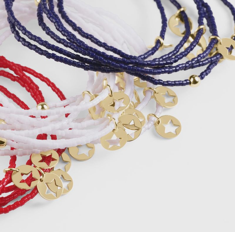 White beaded Hope Classic bracelet with small gold disc charm and 14kt gold accents, styled on wrist in lifestyle setting