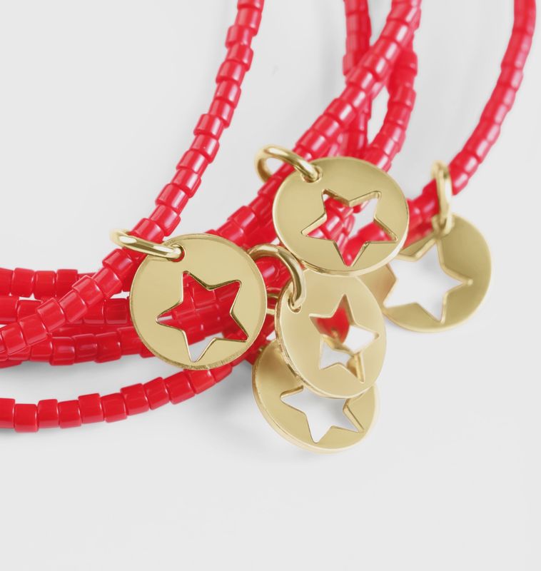 Bright red beaded Hope Classic bracelet with small gold disc charm worn on wrist in lifestyle setting