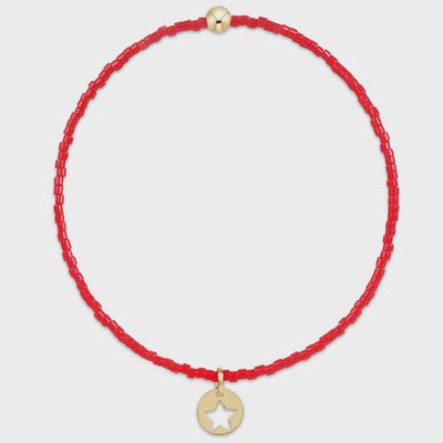 Bright red beaded bracelet with small gold disc charm on white background