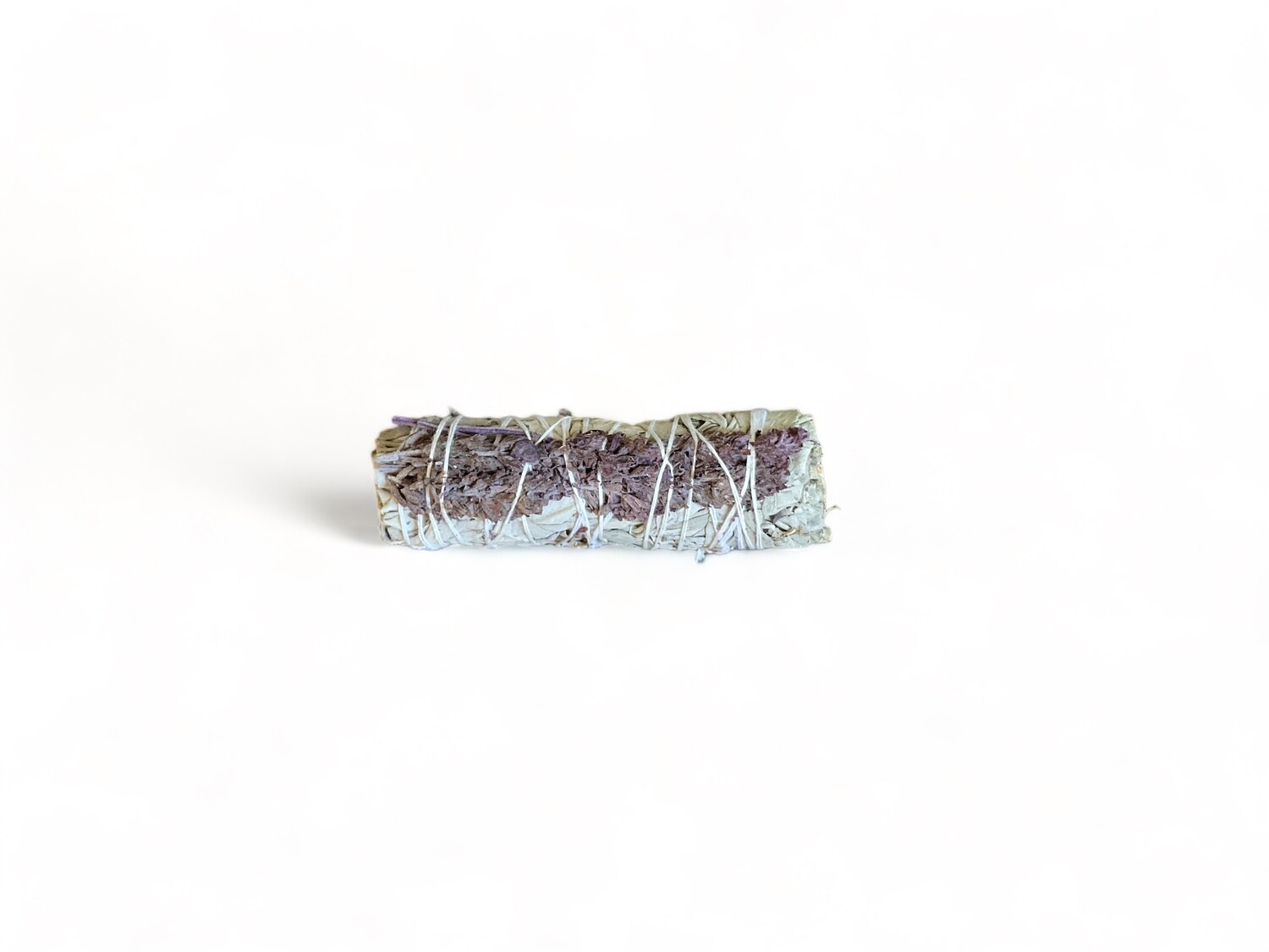 Photo of a four inch smudge stick made from white sage and royal purple lavender flowers. The stick is tightly bound with twine and features a mix of white sage and vibrant purple lavender. Used for energy cleansing and purification, it aims to promote peace and calm through its soothing aroma.