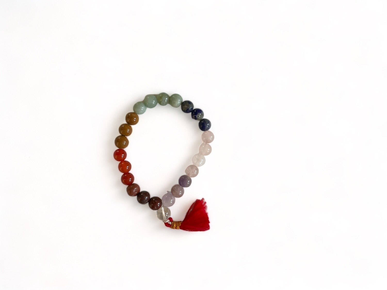 Photo of a stretch bracelet featuring seven distinct stones, each representing one of the seven chakras, arranged in a vibrant sequence. The bracelet is finished with a red tassel, enhancing its colorful and symbolic design, and is designed to balance energy, improve well-being, and promote spiritual harmony.