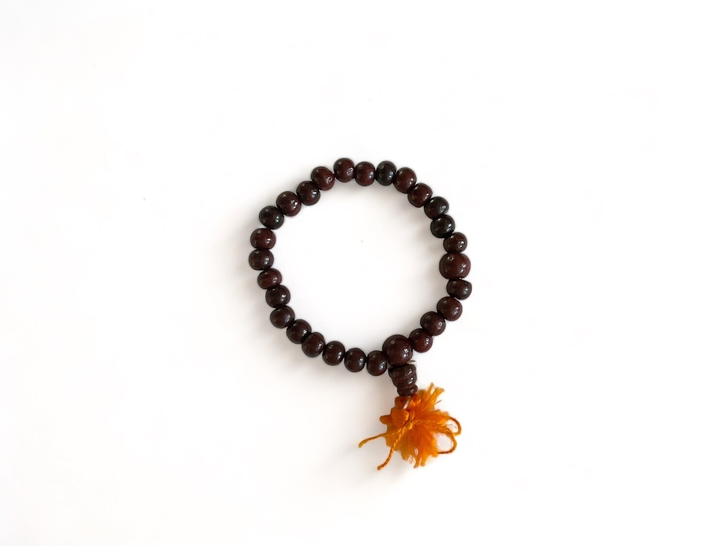 Photo of a rich earthy deep brown Rosewood Mala bracelet with 6mm beads and a bright orange tassel. This piece is designed to support Heart Chakra healing, promoting compassionate energy and spiritual connection.