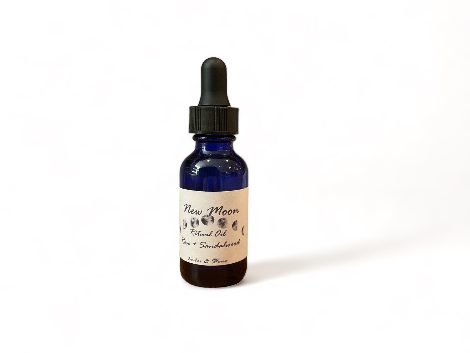 Image of New Moon Oil featuring a blend of rose and sandalwood. The clear dark blue bottle contains a light-colored liquid and is labeled for ritual use. It has a dropper top for precise application. The oil is designed for intentional use, such as applying to stones, candles, and journals, or adding to baths and diffusers. 