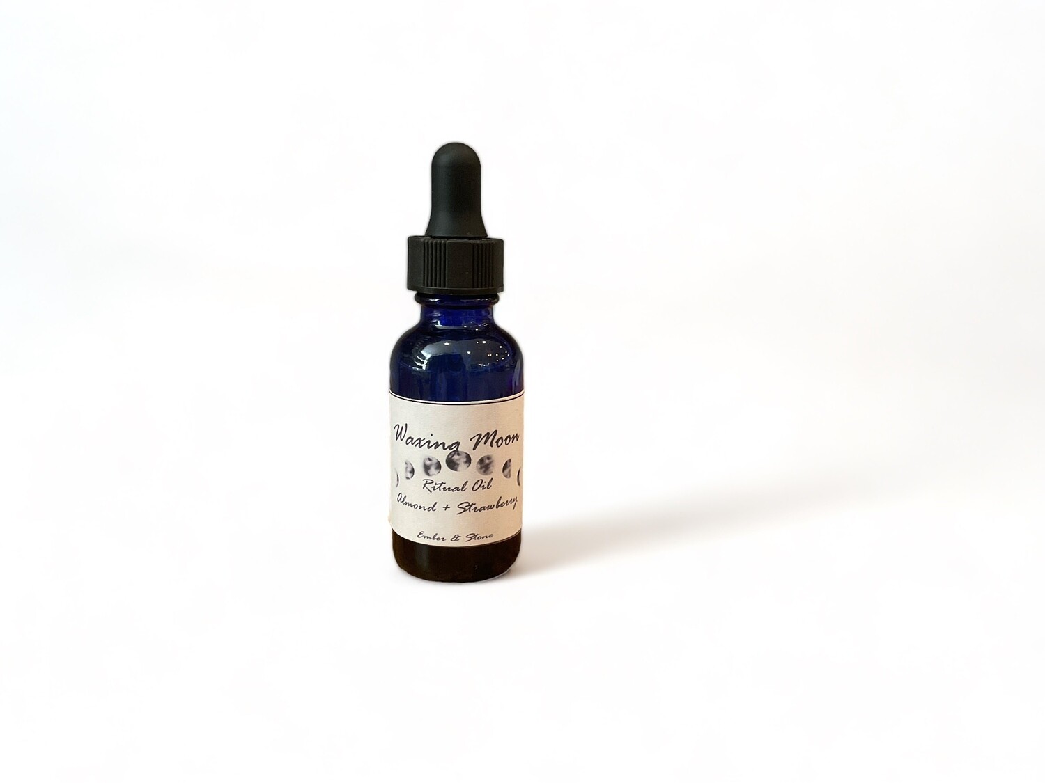 Photo of Waxing Moon Oil, featuring a blend of almond and strawberry. The bottle has a label indicating it is for ritual use. The bottle includes a dropper cap for precise application. The oil is designed for use on candles, stones, journals, or can be added to baths and diffusers. It supports growth and manifestation during the waxing moon phase.
