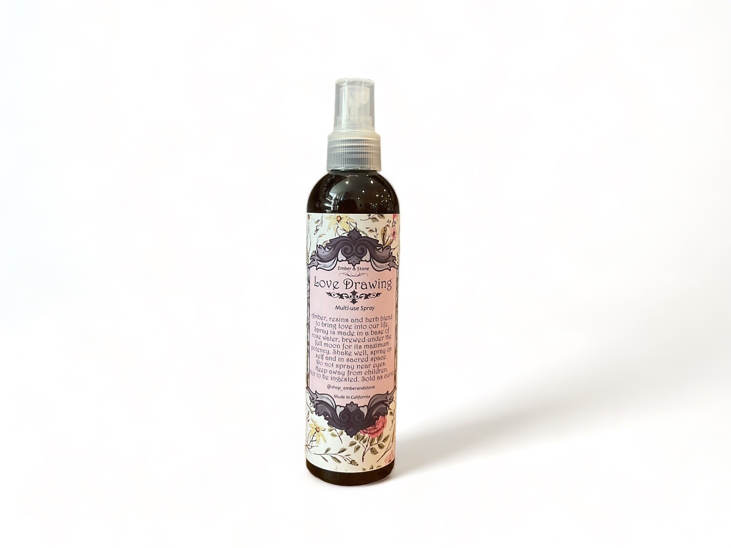 Image of a two ounce bottle of Love Drawing Room Spray. The clear glass bottle features a label stating &#39;Love Drawing Room Spray&#39; and describes it as a rose water mist crafted with herbs and resins under a full moon. The label highlights its purpose to attract love energy and enhance your space. The design emphasizes its metaphysical properties and its role in drawing love.
