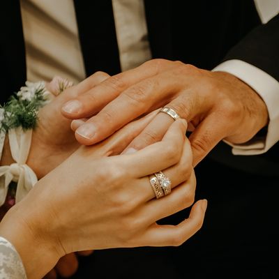 Wedding gifting category at my geisha Milton Keynes UK. A couple holding hands, possibly at a wedding ceremony. The focus is on the hands showcasing wedding rings and jewelry. The setting appears formal and elegant.