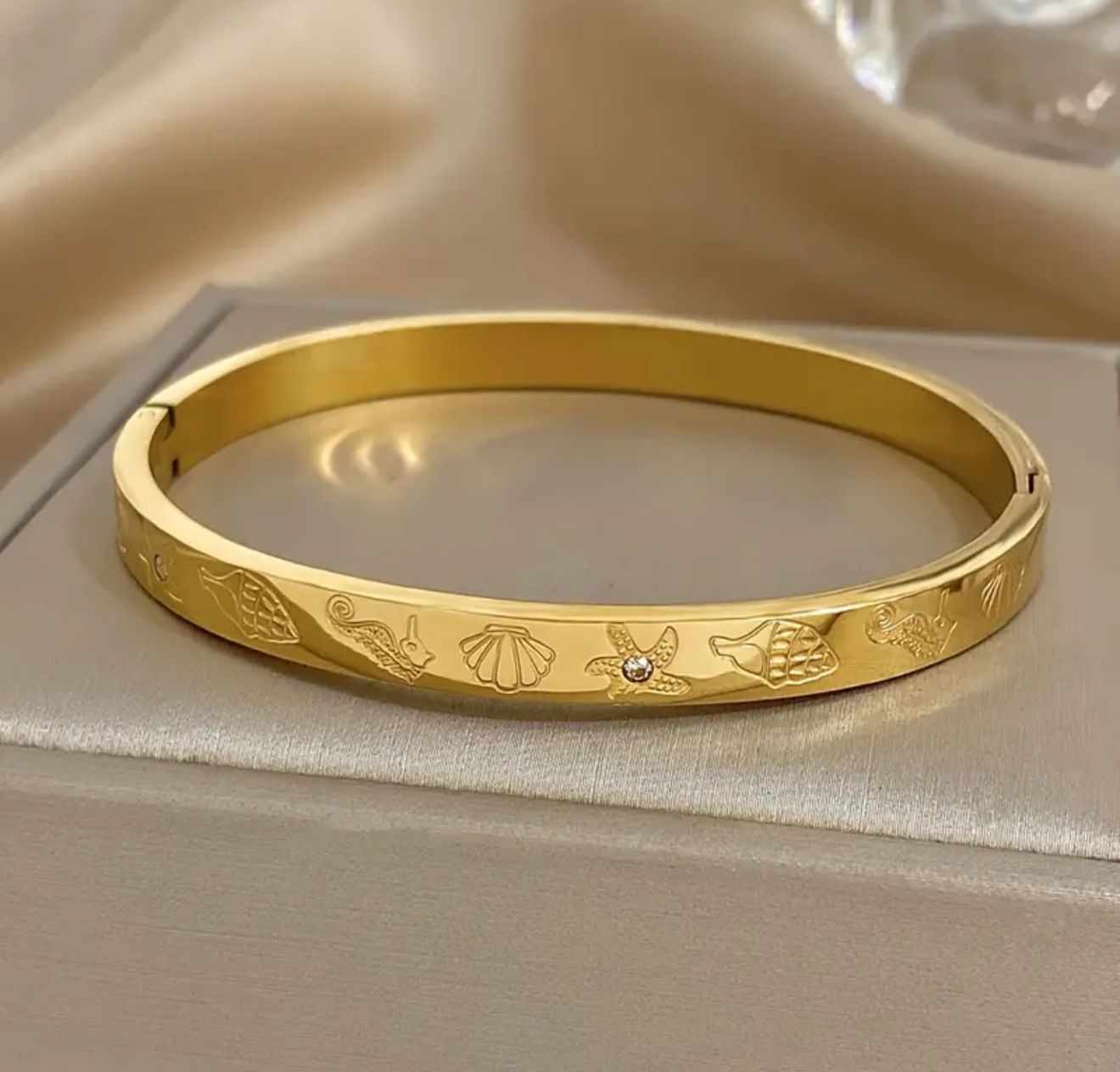 Golden Siren Cuff — A radiant stainless-steel bangle adorned with sculpted seahorse, shell, starfish, and fish motifs. Embellished with luminous rhinestones and finished in waterproof golden polish Golden Siren Cuff — A radiant stainless-steel bangle adorned with sculpted seahorse, shell, starfish, and fish motifs. Embellished with luminous rhinestones and finished in waterproof golden polish