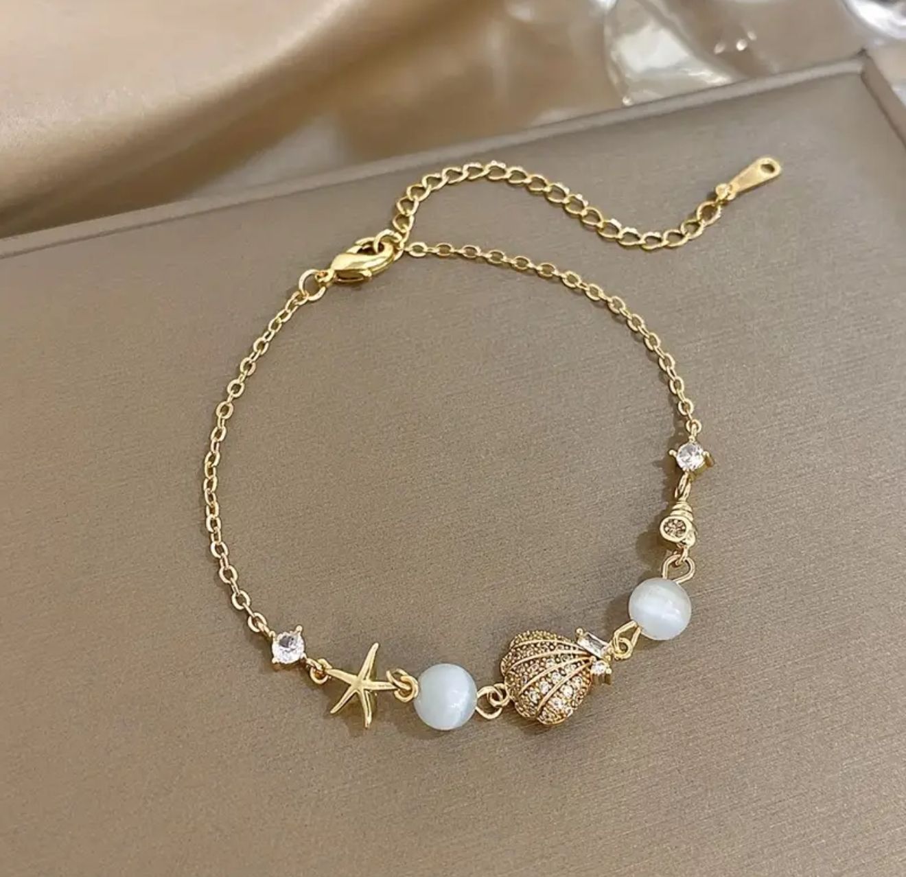 Hide Tides Charm Bracelet — A luminous stainless steel creation adorned with delicate shell, starfish, and conch charms. Finished in a radiant golden tone, this bracelet embodies the elegance of coast Hide Tides Charm Bracelet — A luminous stainless steel creation adorned with delicate shell, starfish, and conch charms. Finished in a radiant golden tone, this bracelet embodies the elegance of coast