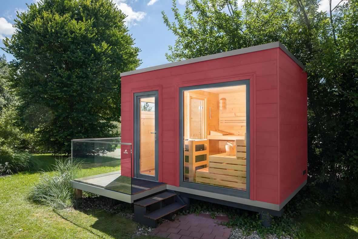 Modernes Saunahaus mit Flachdach und schwedenroter Holzfassade, klare Kubusform und Holz-Aluminium-Fenstern – ein stilvoller Rückzugsort für den Garten.