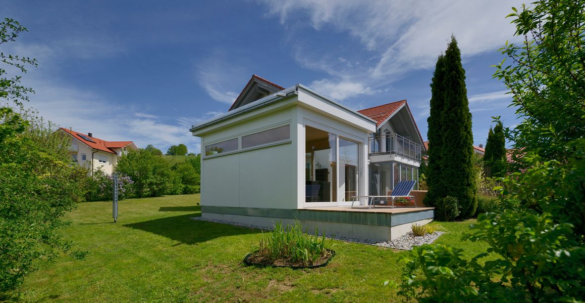 Seitenansicht des rechteckigen Gartenhauses mit klaren Linien und durchgehender Glasfront – ein stilvoller Rückzugsort für Entspannung im Freien.