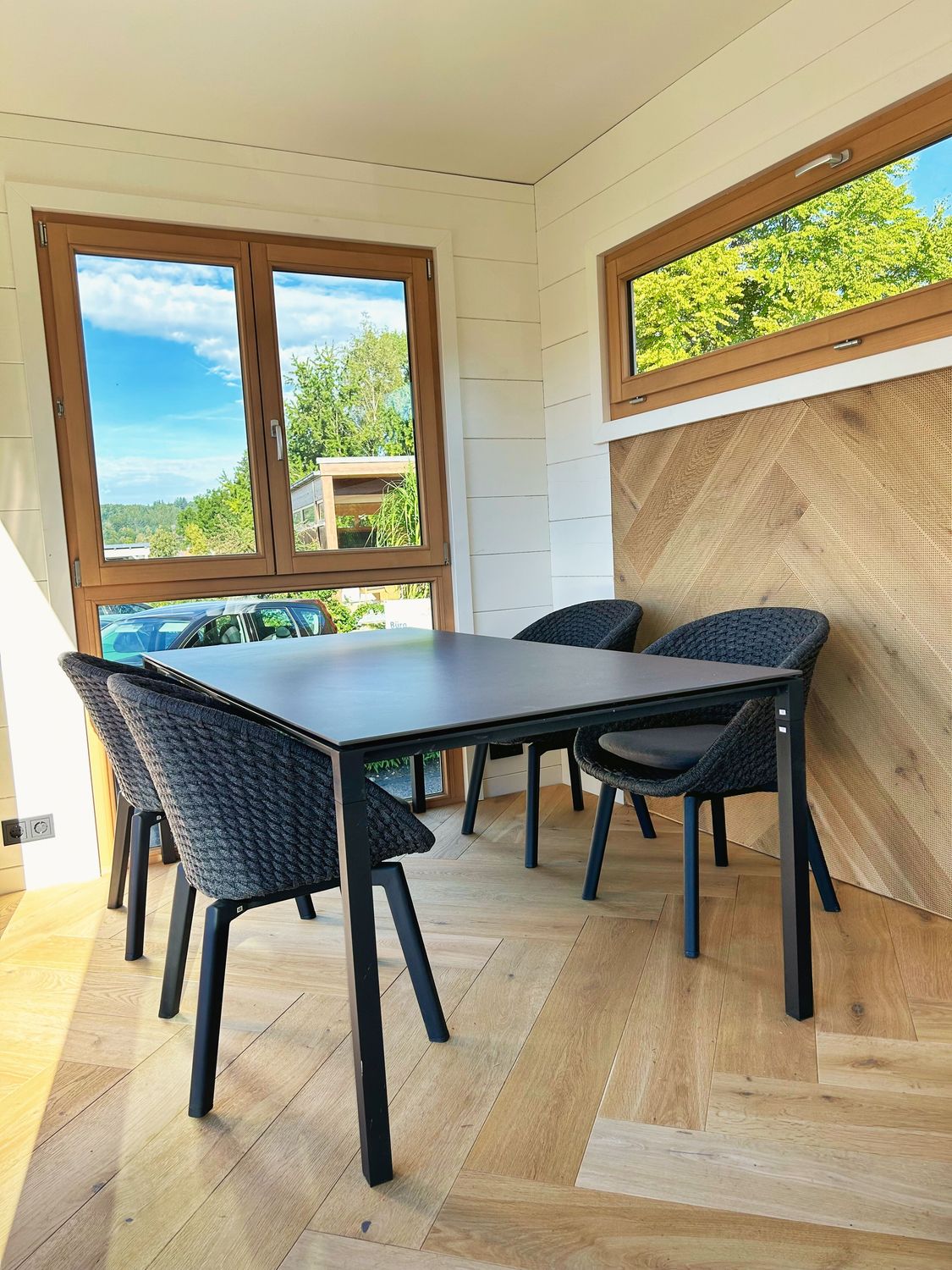 Funktioneller Innenraum mit Schreibtisch, Sitzgelegenheit und Holzverkleidung – Tageslicht durch große Fenster sorgt für ein angenehmes Arbeitsumfeld.