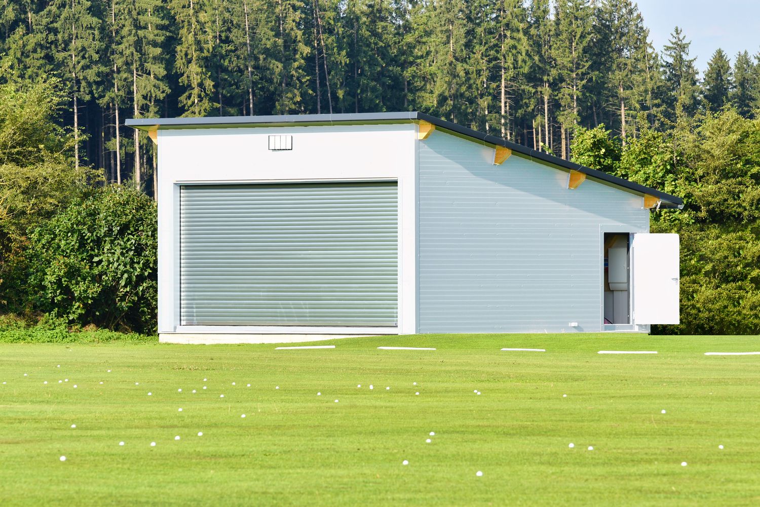 Indoor-Golfhalle aus Holz 8×8 m – moderne Außenansicht mit Rolltor und Stahltür