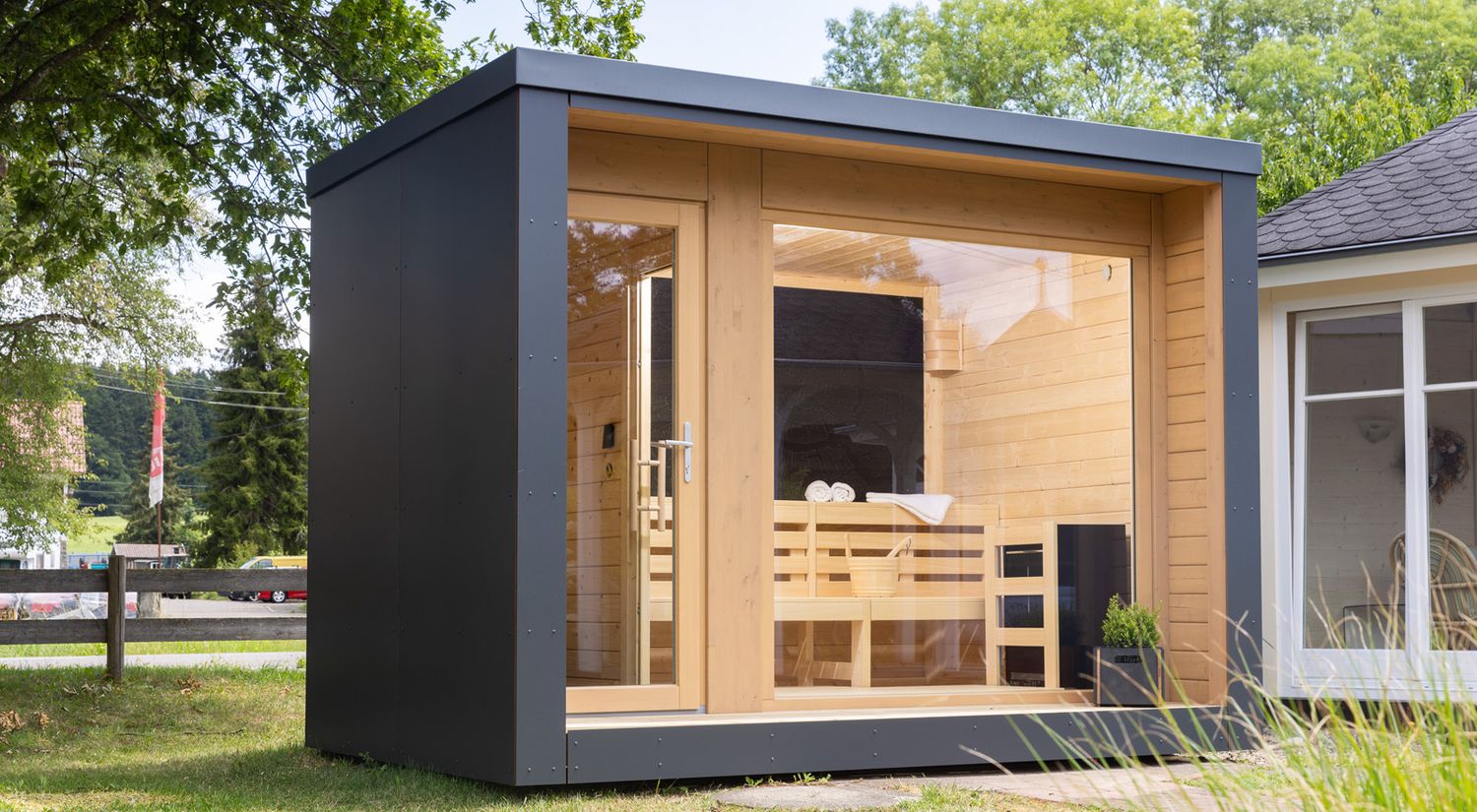  Design-Saunahaus mit 180° Panoramaverglasung, eingebettet in eine grüne Gartenlandschaft – verbindet modernes Design mit natürlicher Umgebung.