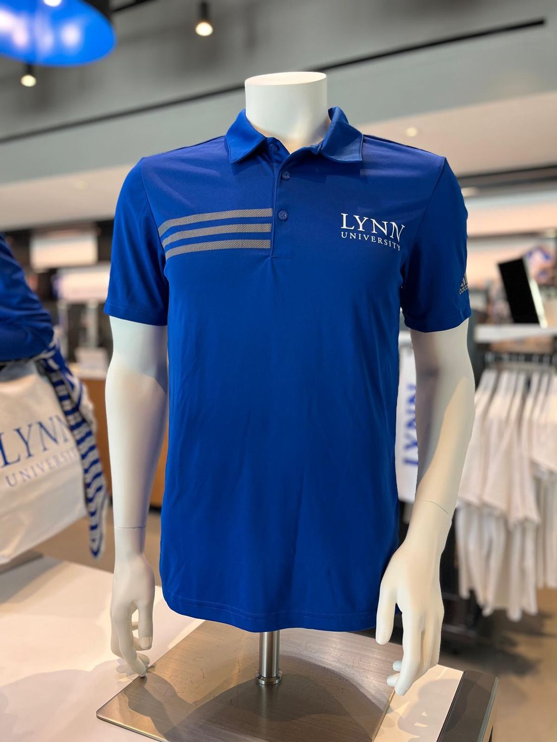 Royal blue short sleeve polo with three gray stripes on right side of chest and text on the left side saying &quot;Lynn University&quot;.