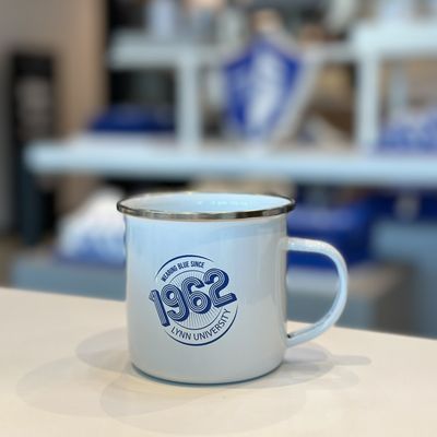 White mug with gold outlining the top of the cup, and a blue 1962 logo on the front.