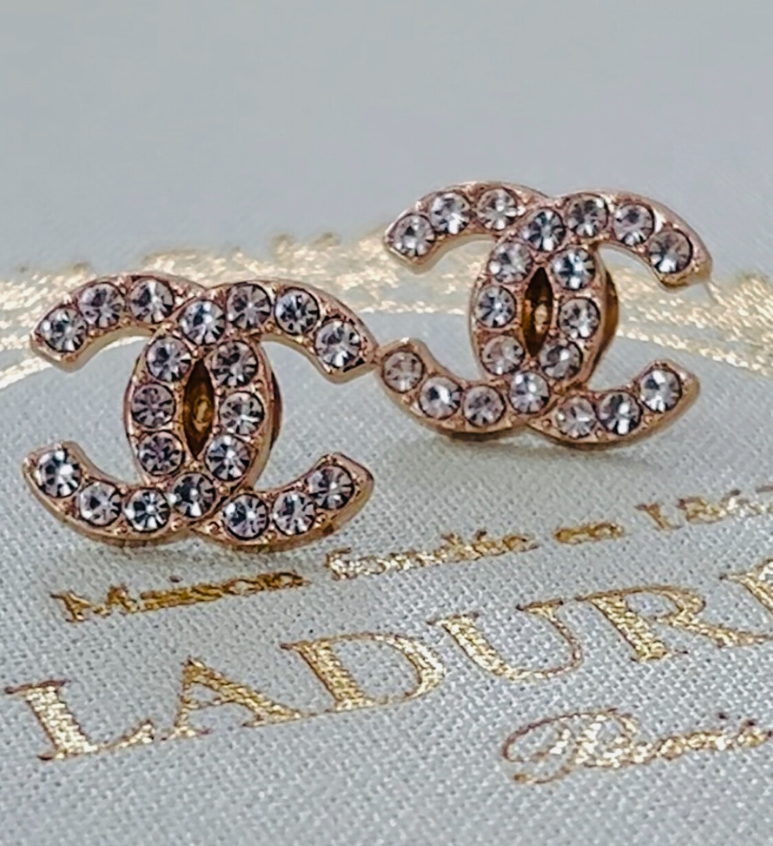 Delicate gold earrings with small rhinestones logo