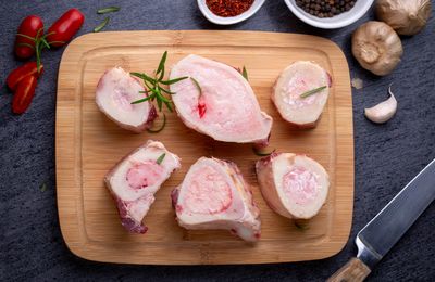 Six cuts of raw Grass-Fed Beef Marrow Bones from Tennessee on a cutting board with rosemary, garlic, and spices.