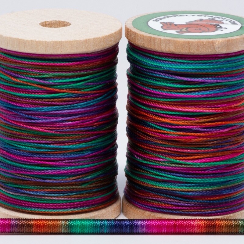 Two Prismatic Charm spools as well as a thin rod wrapped in thread, showing colors.