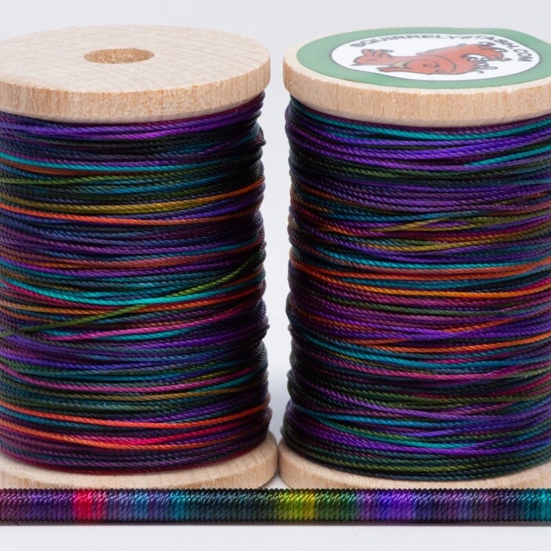 Two spools of Cosmic Blast thread with a thin rod wrapped in thread, displaying variegated colors.