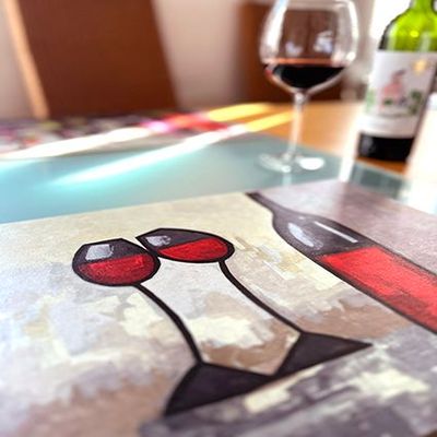 Vinyl Tischset mit Rotweinflasche, zwei Gläsern Rotwein, auf einem Tisch dekoriert, mit echtem Rotwein im Hintergrund.