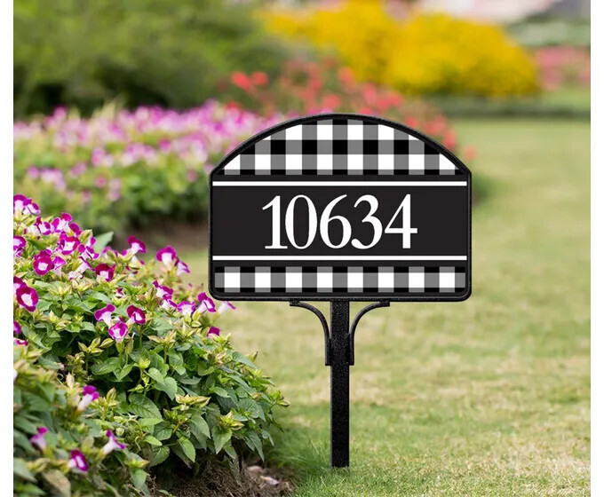 Black and white check magnetic yard sign with address numbers, installed on a metal stake in a garden.