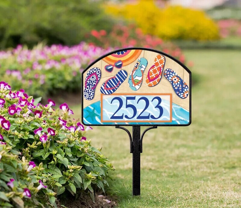 Magnetic yard sign featuring colorful patterned flip flops and address numbers, installed in a garden.