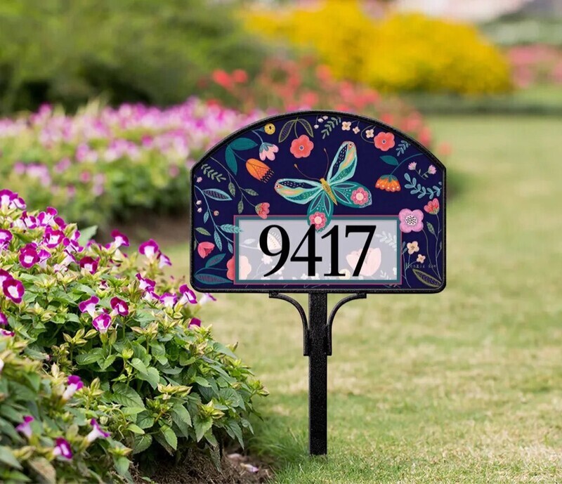 Butterfly and floral magnetic yard sign displaying address numbers, installed on a metal stake in a garden.