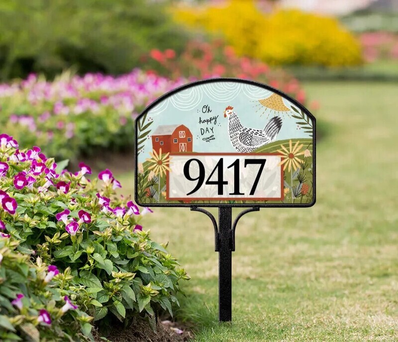 Magnetic yard sign featuring a rooster, red barn, sunflowers, and address numbers installed in a garden.