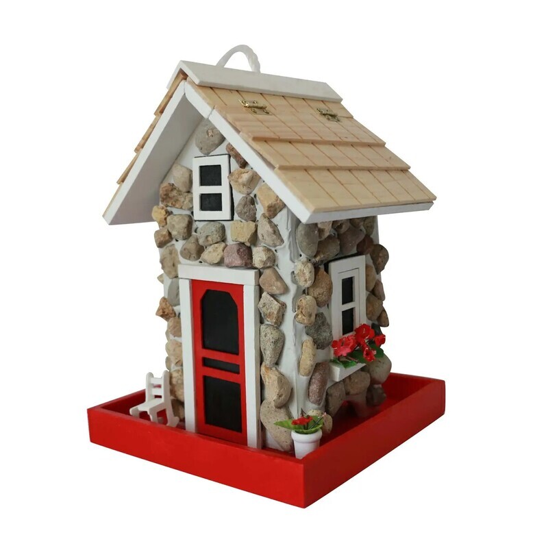 Fieldstone cottage bird feeder with a red door, white window trim, and a small rocking chair on a stone-textured porch.