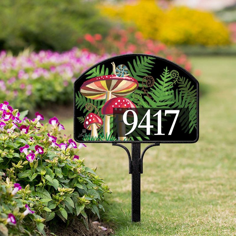 Magnetic yard sign featuring a mushroom, snails, ferns, and address numbers, installed in a garden setting.