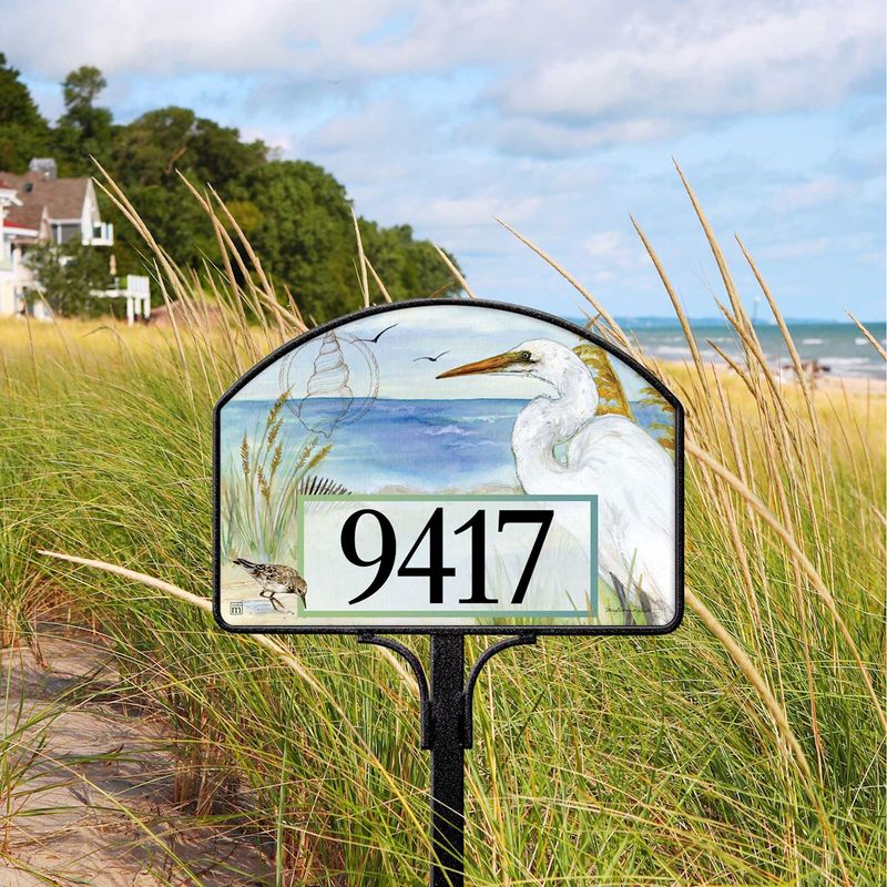 Magnetic yard sign featuring a white egret in marsh grass and address numbers, installed in a garden.