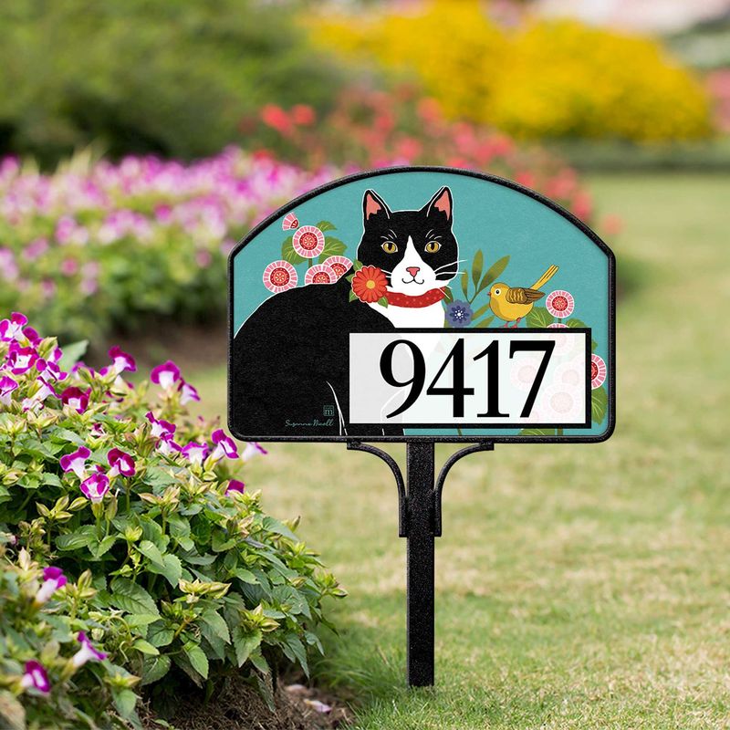 Magnetic yard sign featuring a black and white cat, pink flowers, and address numbers, installed in a garden.