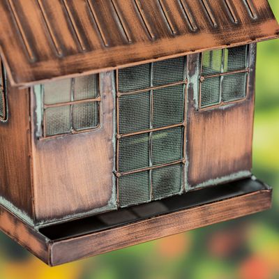 Close-up of the antique copper cottage birdhouse showing textured siding and a small door.