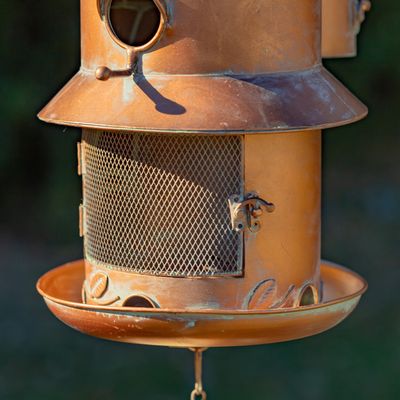 Close-up of the antique copper birdhouse showing the mesh seed reservoir and the small round entry hole