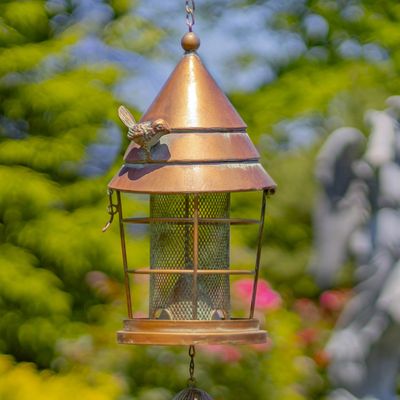 Close-up of the antique copper bird feeder showing the mesh seed cylinder and decorative metal mushroom accents.