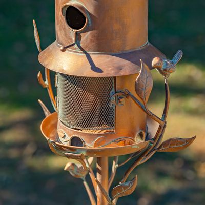Close-up of the handcrafted copper Homestead birdhouse and mesh bird feeder.