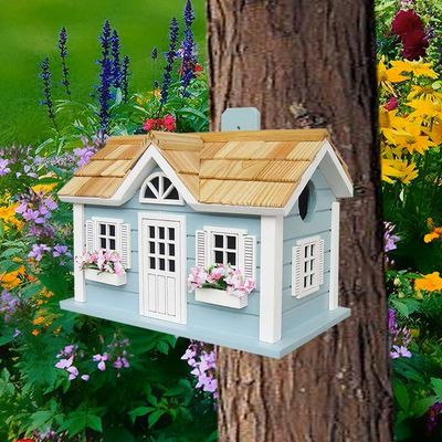 Handcrafted blue cottage birdhouse with floral window boxes hanging from a tree