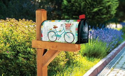 Blue Bike patterned mailbox cover installed on a wooden post in a green garden.