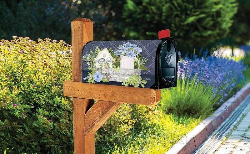 Farmhouse floral mailbox cover installed on a wooden post in a lush green garden setting.