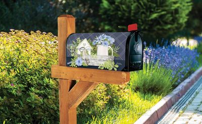Farmhouse floral mailbox cover installed on a wooden post in a lush green garden setting.
