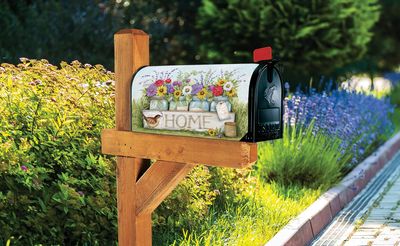 Welcome Home floral mailbox cover installed on a wooden post in an outdoor garden setting.