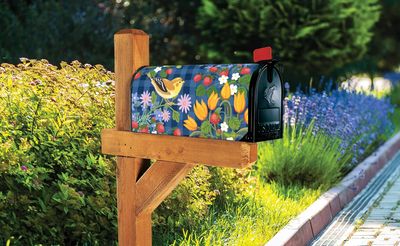 Strawberry floral mailbox cover installed on a wooden post in a garden setting.