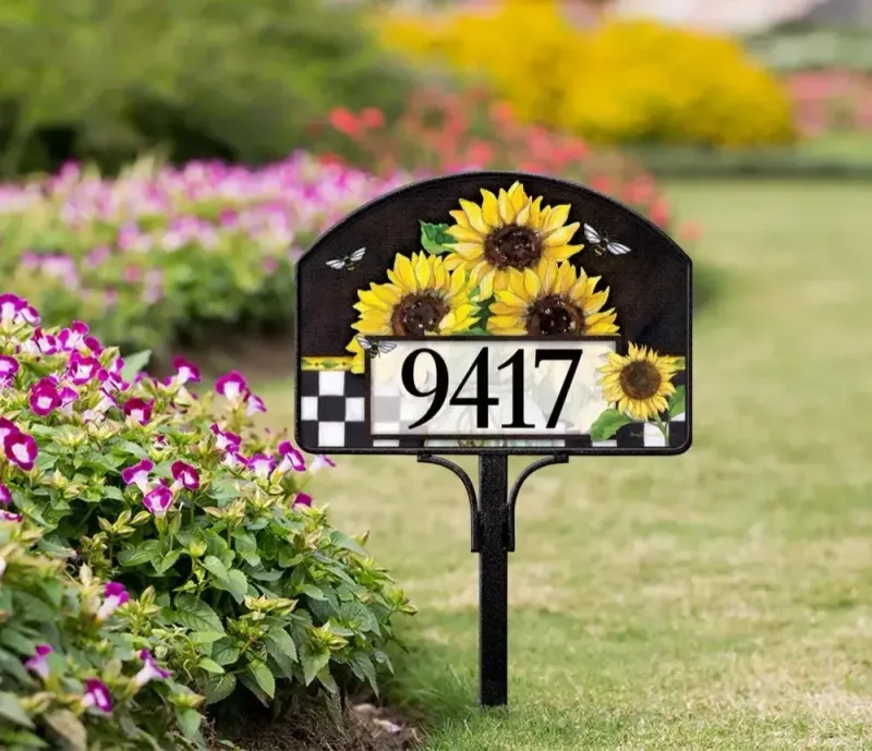 Magnetic yard sign featuring bright sunflowers and address numbers, installed on a metal stake in a garden.