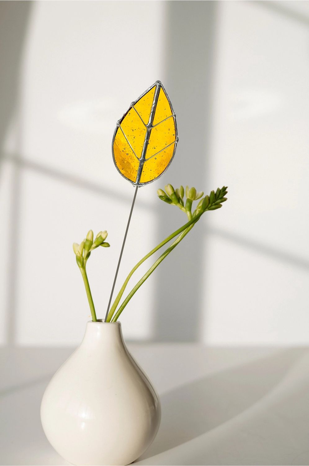 Amber oval stained glass leaf plant pick on a thin metal stem displayed in a small vase with green stems.