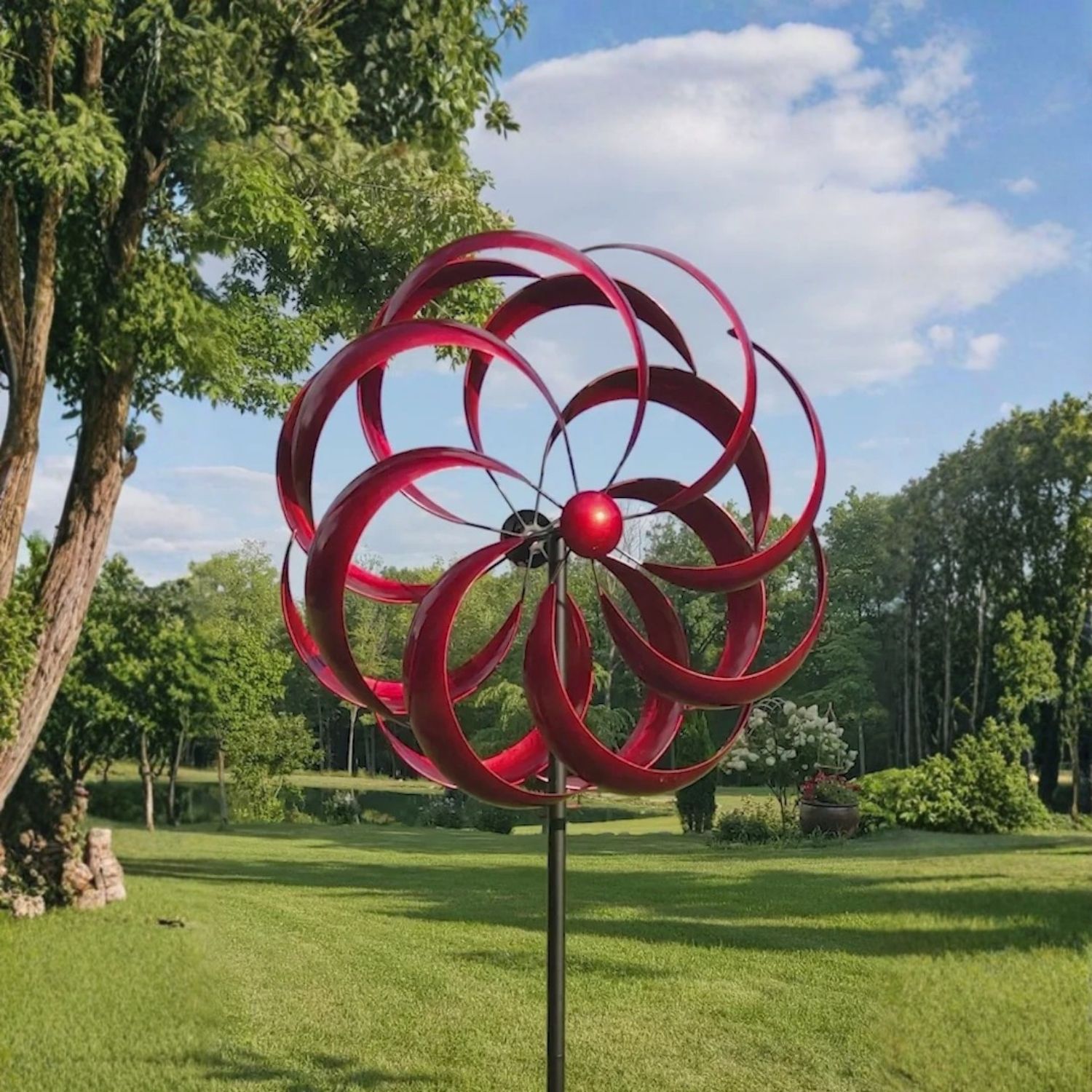 Red metal dual-rotating wind spinner on tall black garden stake displayed in a grassy yard.